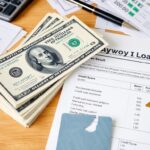 A stack of hundred-dollar bills, a calculator, a pen, broken credit cards, and financial documents—including a loan agreement and US credit scores sheet—are spread out on a wooden table, hinting at payday loans or debt concerns.