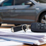 Car keys resting on a stack of car loan collateral documents with a gray car in the background.