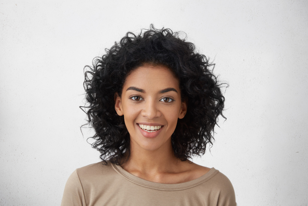 Smiling young woman with curly hair thinking about payday loans against a light background.